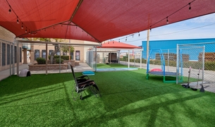 Outdoor play yard with shade sails, a trampoline and artificial turf